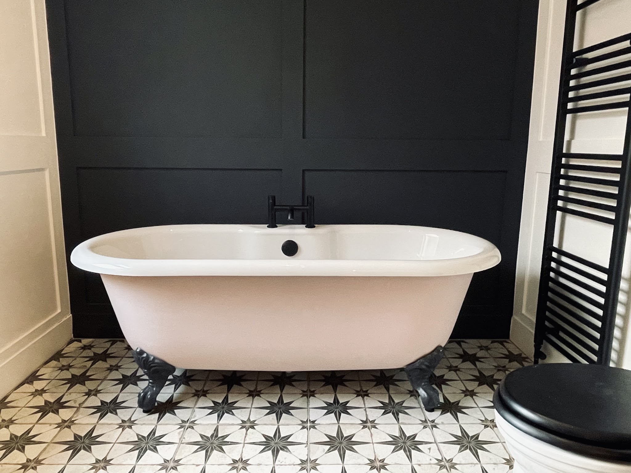 Roll top bath against a dark panelled wall with star pattern floor tiles