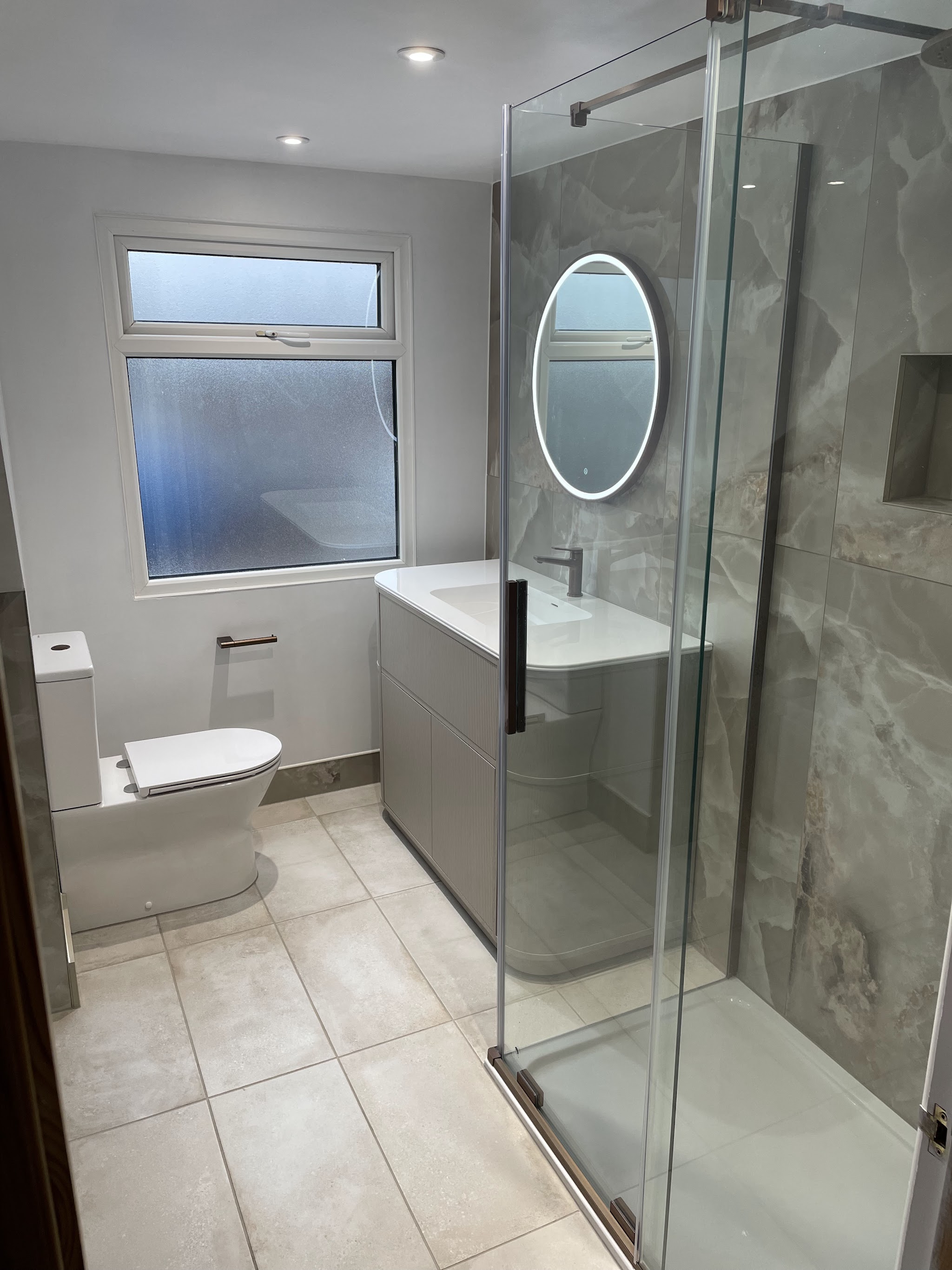 Walk-in shower with large marble effect tiles and an illuminated mirror