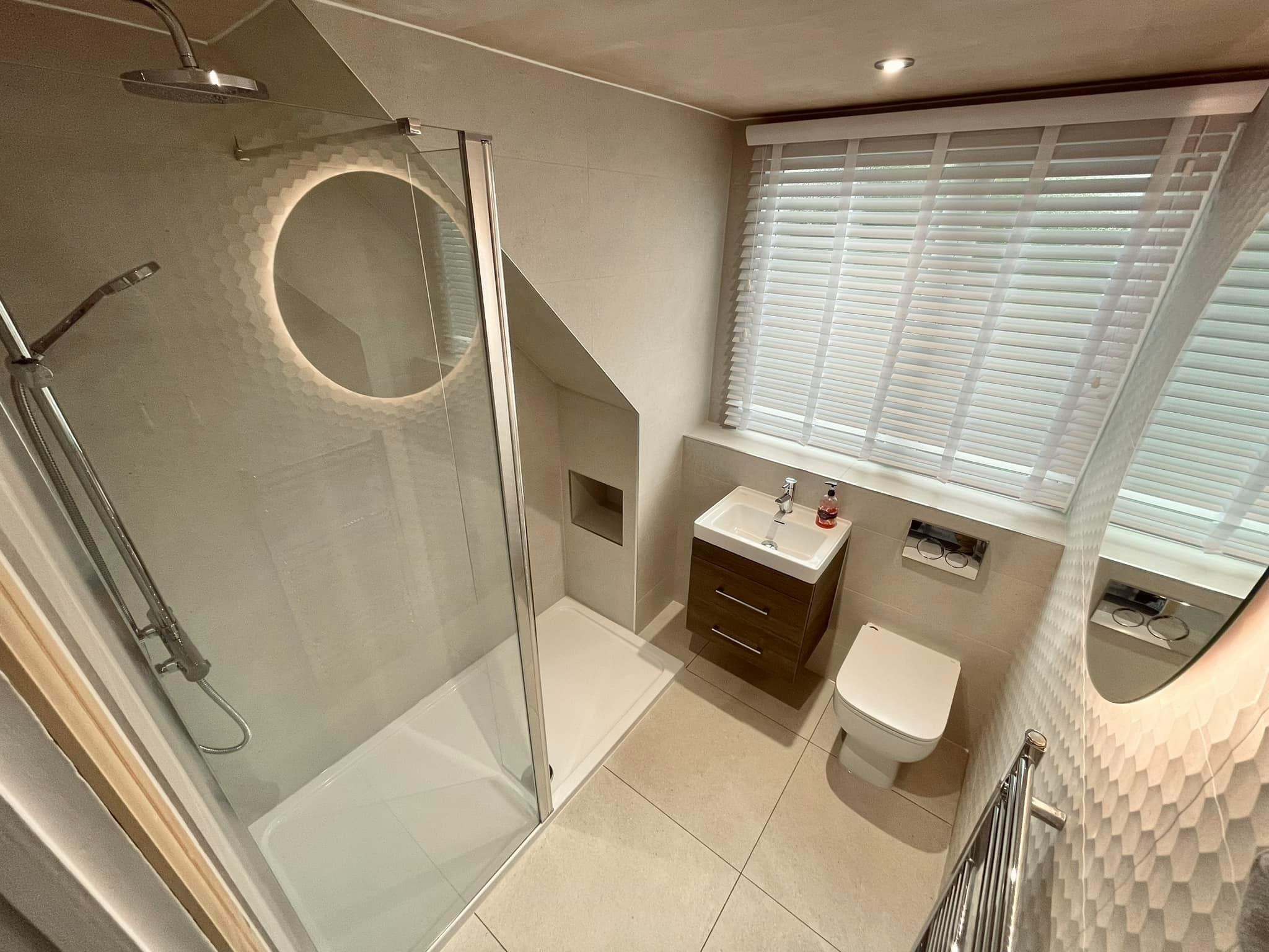 Finished loft shower room with an illuminated round mirror and wall hung toilet