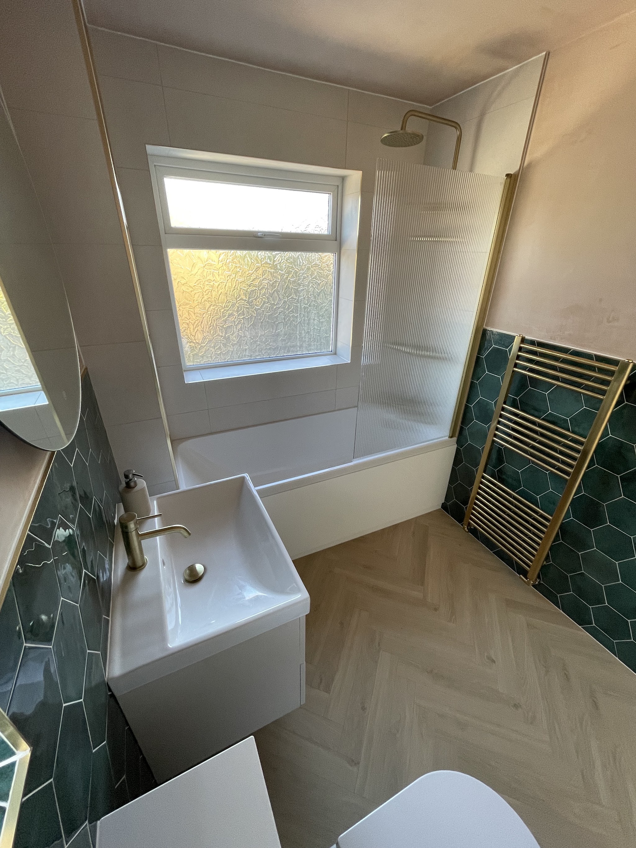 Bathroom with green hexagon tiles, brass towel rail and herringbone floor