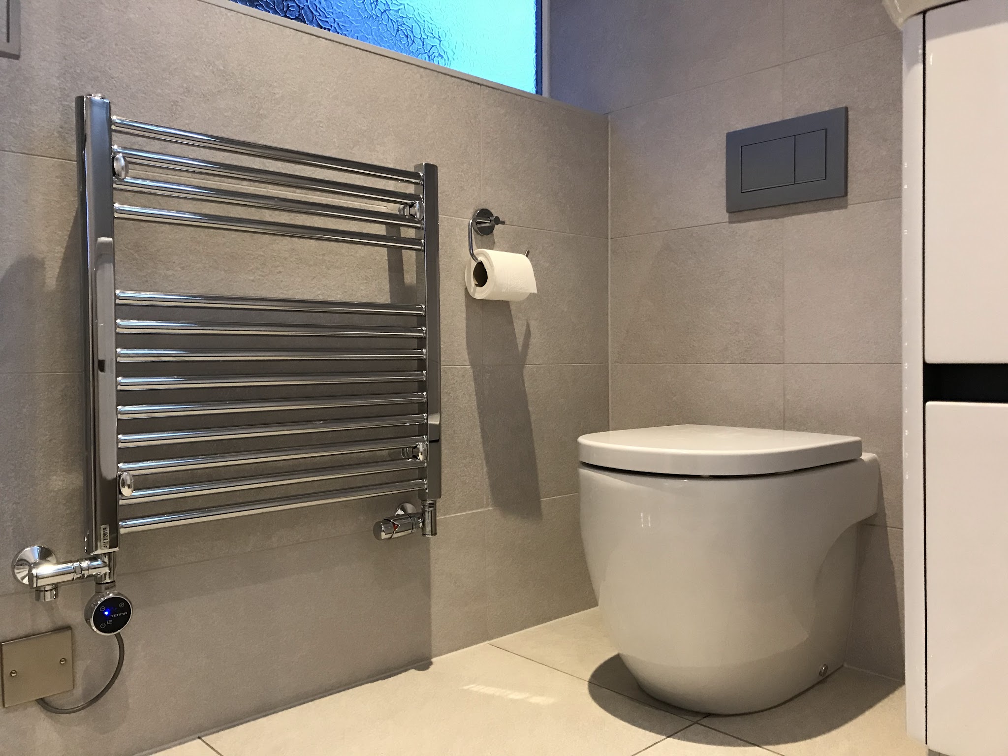 Wall hung toilet and chrome heated towel rail on grey tiles