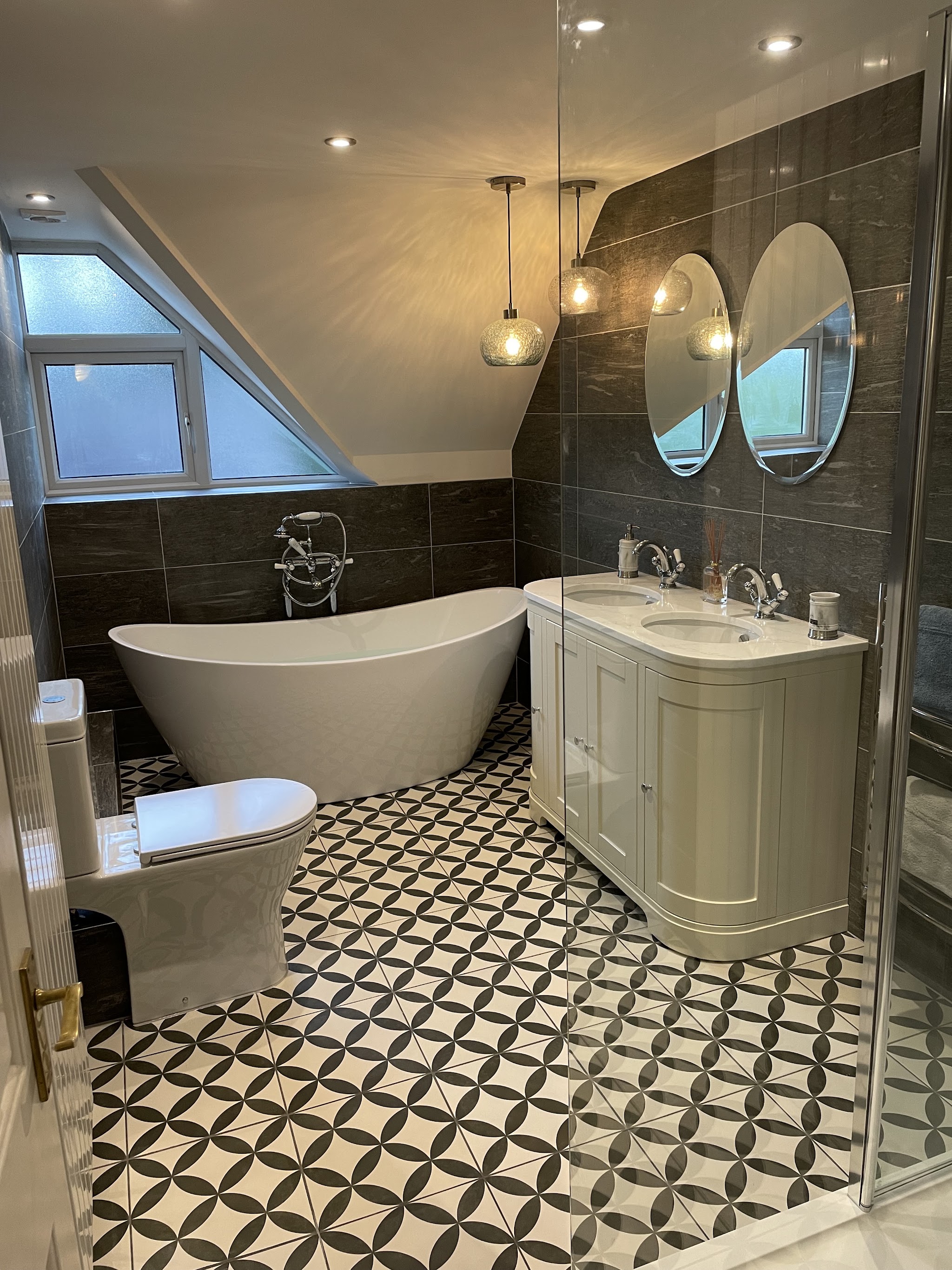 Bathroom with a freestanding bath, double vanity and twin oval mirrors under a sloping ceiling